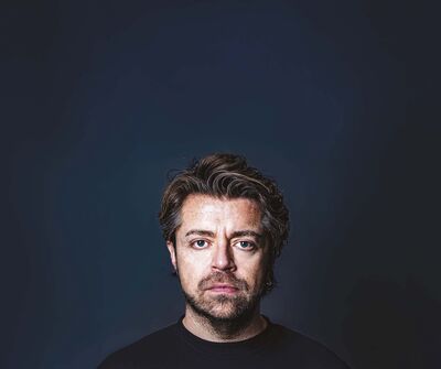 Daan staat voor een blauwe achtergrond en kijkt strak de camera in. 