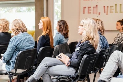 Zij aanzicht van zes vrouwen op stoelen die in de vergaderruimte geconcentreerd luisteren. 