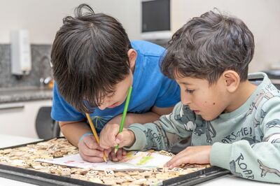 Twee kinderen buigen zich samen over een tekening en kleuren enthousiast verder